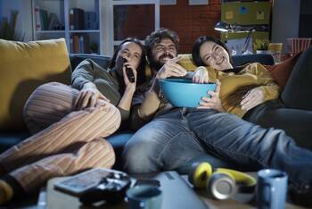 Drei Personen sitzen auf Couch und schauen auf Fernseher