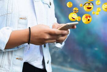 Person tippt auf Smartphone, aus welchem Emojis fliegen