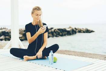 eine Frau sitzt auf einer YogaMatte mit deinem Smartphone in der Hand
