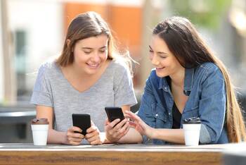 Zwei Frauen zeigen sich etwas auf ihren Smartphones beim Kaffee
