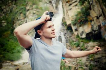 Junger Mann mit Go pro auf Kopf vor Wasserfall