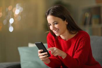 Frau im roten Pullover schaut lächelnd auf Smartphone