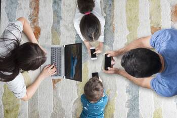 Eine Familie liegt auf dem Teppichboden und jeder schaut auf ein mobiles Endgerät