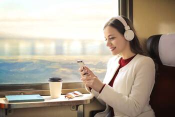 Frau sitzt in Zug mit Kopfhörern auf und schaut auf Smartphone-Display