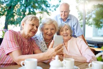 Mehrere ältere Personen schauen gemeinsam fröhlich auf ein Smartphone Display