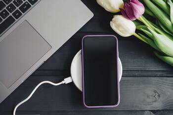 Smartphone liegt auf kabelloser Ladestation umgeben von Tulpen und einem Macbook