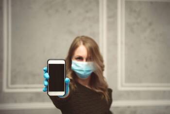 Frau mit Gesichtsmaske hält iPhone in die Kamera