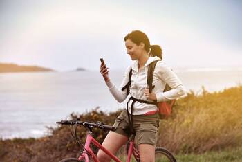 Sportlich gekleidete Frau auf Fahrrad in der Natur schaut auf Smartphone