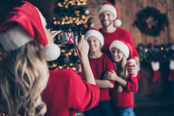 Frau macht Foto von ihrer Familie  vorm Weihnachtsbaum mit ihrem Smartphone