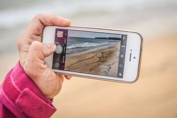 Person macht mit iPhone Foto am Strand