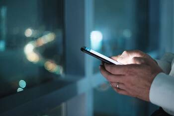 Zwei Hände in Business-Umgebung bei Nacht halten Smartphone