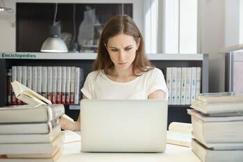 Frau guckt mit offenem Buch in der Hand konzentriert auf ihren Laptop
