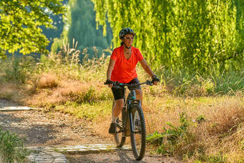 Frau fährt auf E-Crossbike über Natur-Radweg.