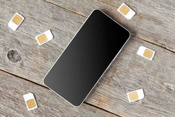 Smartphone liegt auf Holzboden umgeben von SIM-Karten