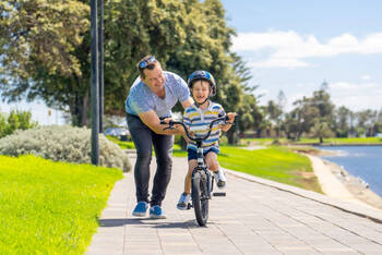 Ein Vater bringt seinem lachendem Kind Rad fahren bei