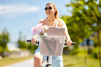 Frau fährt auf Rad mit Fahrradkorb durch eine sonnige Landschaft