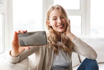 Frau hält Smartphone vor ihrem Gesicht und lächelt