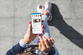 Person mit pink lackierten Fingernägeln tippt auf Smartphone mit geöffneter Twitter-Anwendung