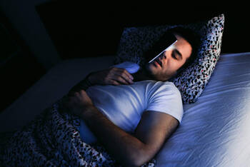 Mann liegt im Bett mit Handy auf dem Gesicht