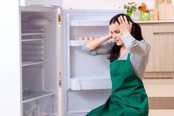Mensch steht mit Händen über den Kopf geschlagen vor geöffnetem Kühlschrank