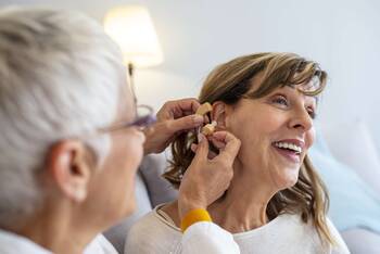 Frau nimmt am Ohr einer anderen Frau Anpassungen am Hörgerät vor