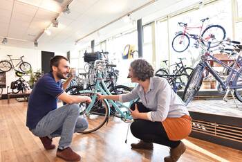 Zwei Personen, ein Kunde und der Verkäufer, befinden sich in einem Fahrradgeschäft. Der Kunde lässt sich vom Fachhändler beraten. 