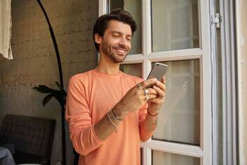 ein Mann steht am Fenster und lächelt in sein Smartphone