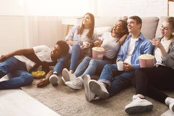 Personengruppe sitzt gemütlich in Wohnzimmer und schaut auf Fernseher