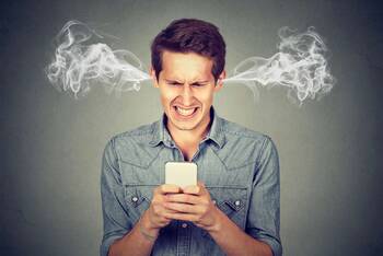Mann guckt verärgert auf sein Smartphone, während ihm Rauchwölkchen aus den Ohren steigen