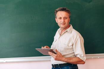 Lehrer hält Tablet in der Hand mit Tafel in Hintergrund