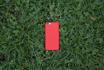 iPhone mit roter Hülle liegt im Gras