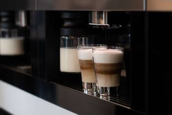 Zwei Gläser gefüllt mit Kaffeespezialität stehen unter Automat