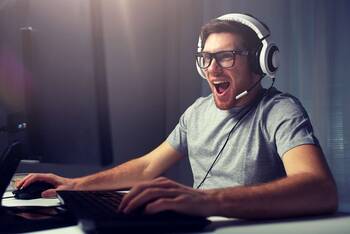 Mann mit Headset sitzt freudig vor Gaming Laptop