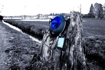Wasserkraftwerk von Blue Freedom mit einem angeschlossenen Smartphone hängt an einem Baumstumpf. Im Hintergrund fließt ein Bach