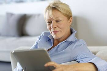 Frau in hellblauem Hemd schaut entspannt auf Tablet