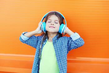 Kind mit blauen Kopfhörern vor gelbem Hintergrund freut sich