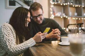 Zwei Menschen schauen gemeinsam lächelnd auf Smartphone Display