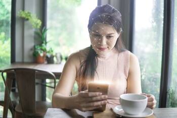 Eine Frau trinkt einen Kaffee und schaut dabei auf ihr Smartphone