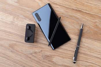 Samsung Galaxy Note 10 liegt neben Bluetooth-Kopfhörern und Stift mit der Rückseite nach oben auf einem Holztisch