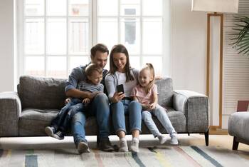 Familie mit zwei Kindern sitzt auf Sofa und schaut auf Smartphone