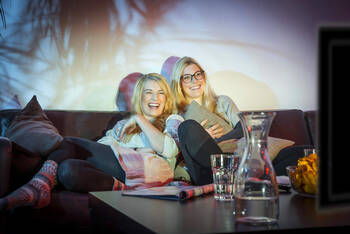 Zwei Frauen sitzen zusammen auf dem Sofa und schauen einen Film