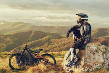 Downhill-Biker sitzt mit Schutzkleidung auf einem Fels