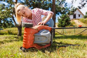 Eine Frau guckt sich die Unterseite eines Rasenmähers an