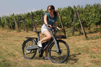 Frau sitzt auf E-Bike vor einem Weinfeld.