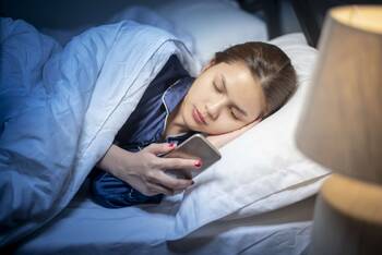 eine Frau liegt im Bett und schaut auf ihr Smartphone