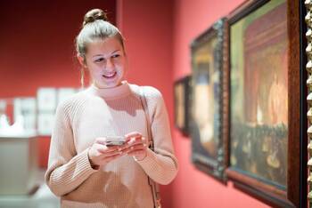 Mann fotografiert lächelnd mit dem Smartphone ein Bild in einem Museum