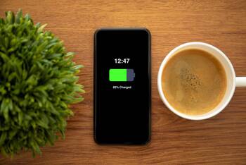Ladendes Handy liegt ohne Kabel auf Tisch zwischen Plastikpflanze und Kaffeetasse