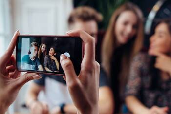 Person macht ein Foto von drei Jugendlichen mit dem Smartphone