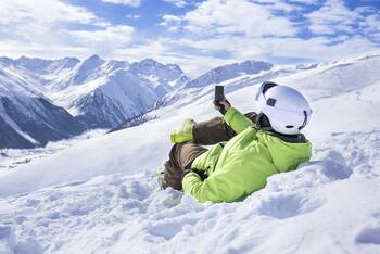 Person liegt in den Bergen im Schnee und guckt auf sein Handy
