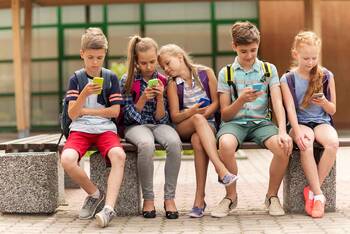 Schulkinder sitzen auf Bank und schauen auf ihre Smartphones